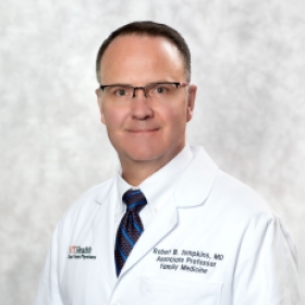 man in a white coat, wearing glasses and smiling
