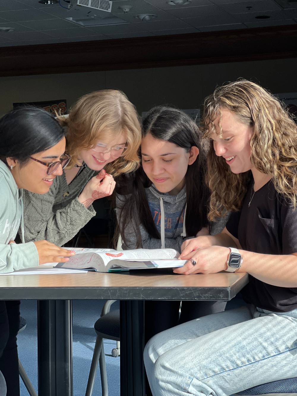 Three students lean in around a desk, focused on a shared document.