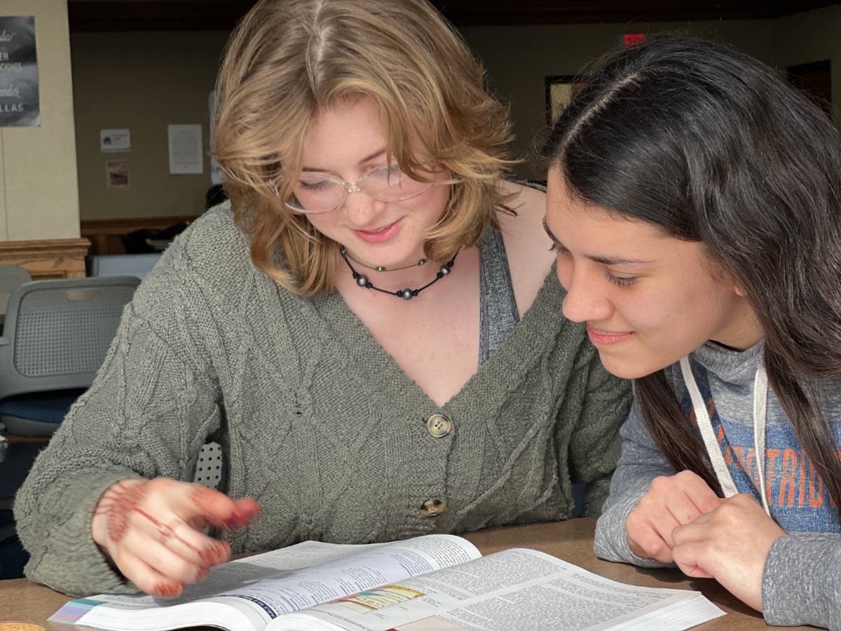 A peer tutor works individually with a student, pointing toward their notes.