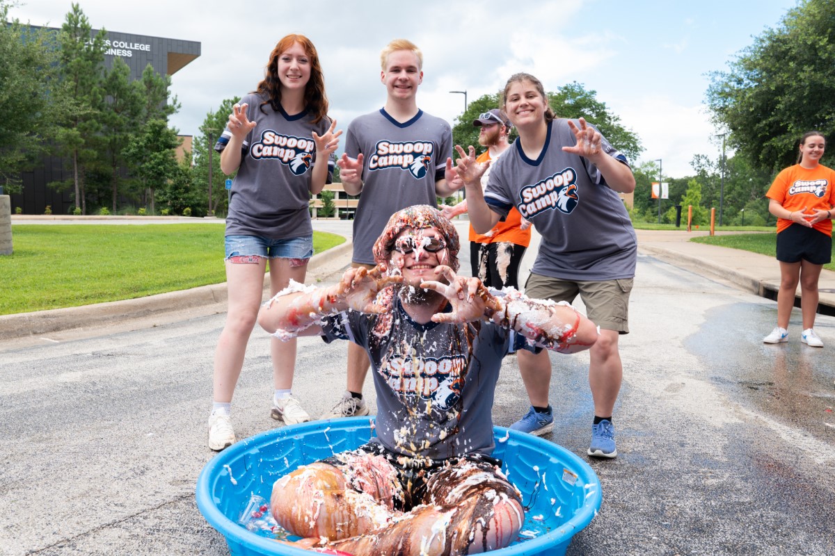 Three students standing behind a student in a mini pool of water smiling